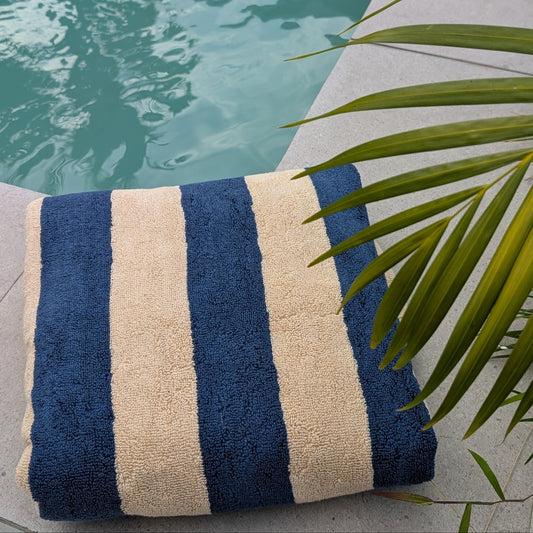 A striped terry cloth towel with navy blue and cream vertical stripes, placed next to a swimming pool.