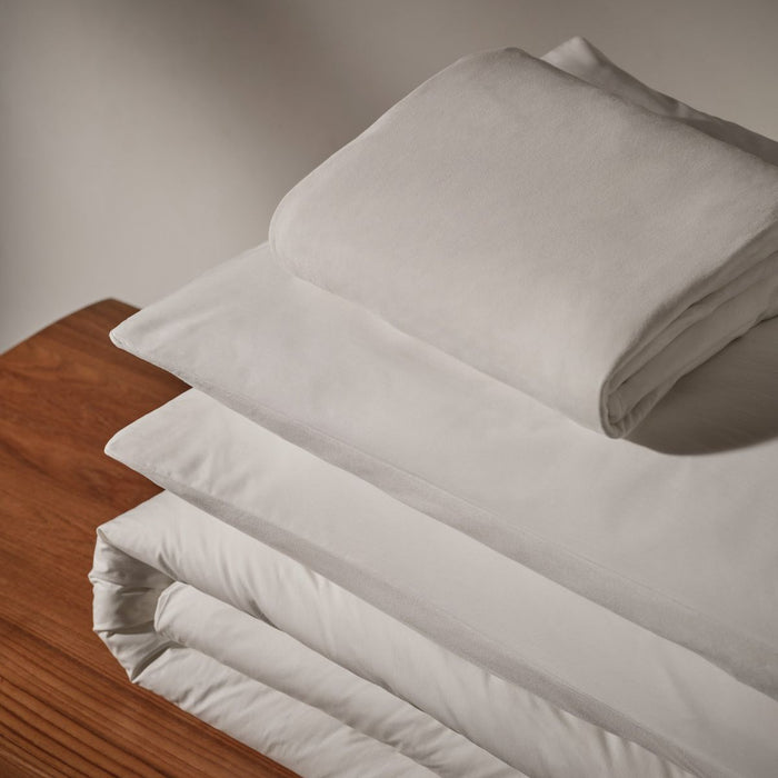White pillows and duvet cover bundle with a white sheet on top made of cotton on a wooden plank underneath