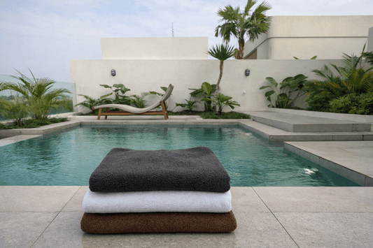 Three folded towels: a dark charcoal gray towel on top, a white towel in the middle, and a brown towel at the bottom.