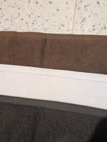 Folded bath mats showing three colors: a dark brown, a wide white middle band, and a dark charcoal gray bottom sectio