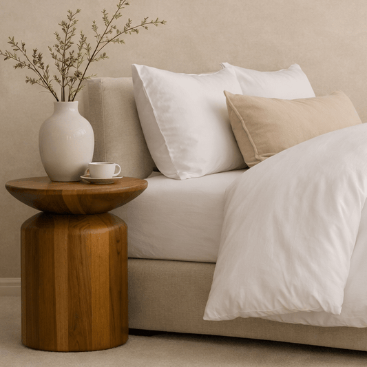 A styled bedroom scene showing a bed with white bedding and pillows, a beige upholstered headboard and footboard.