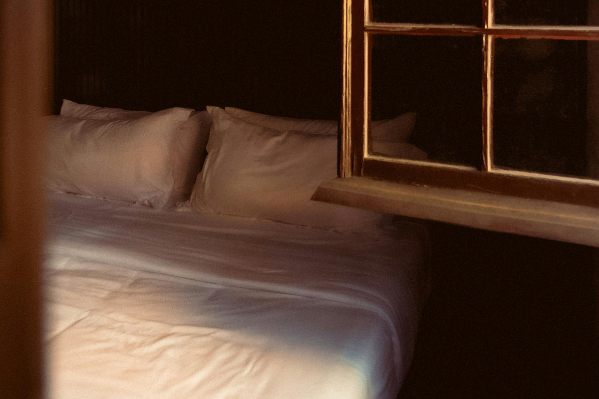 Bed with pillows in a dimly lit room with a window.